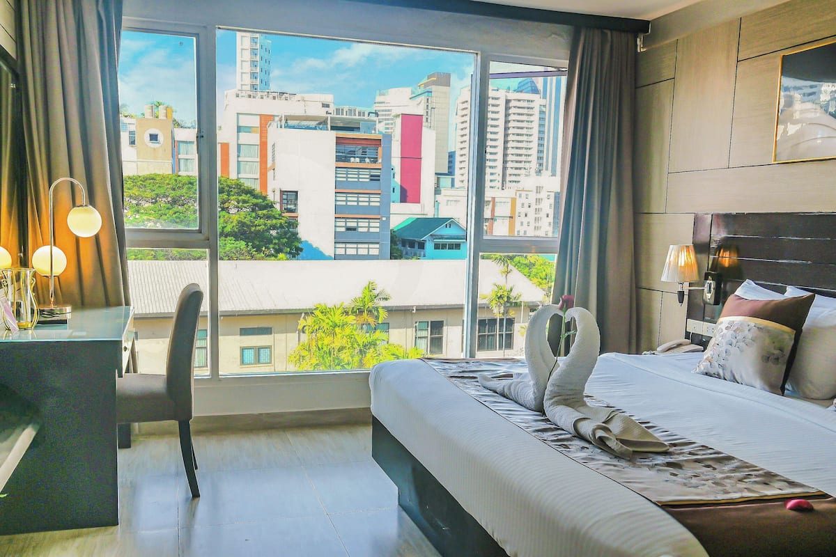 A hotel room with a large window, a bed, a desk, and a chair.