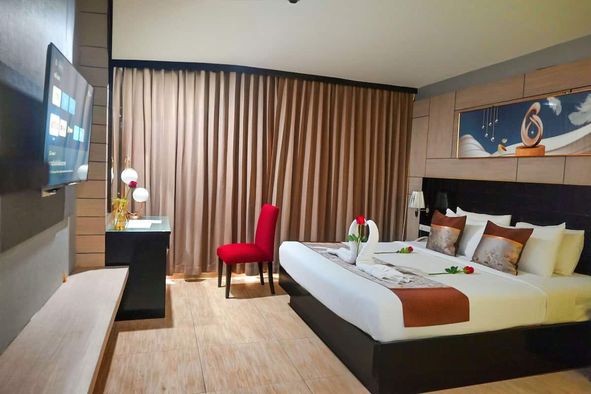 A hotel room with a bed, a desk, a chair, a TV, and a painting on the wall.