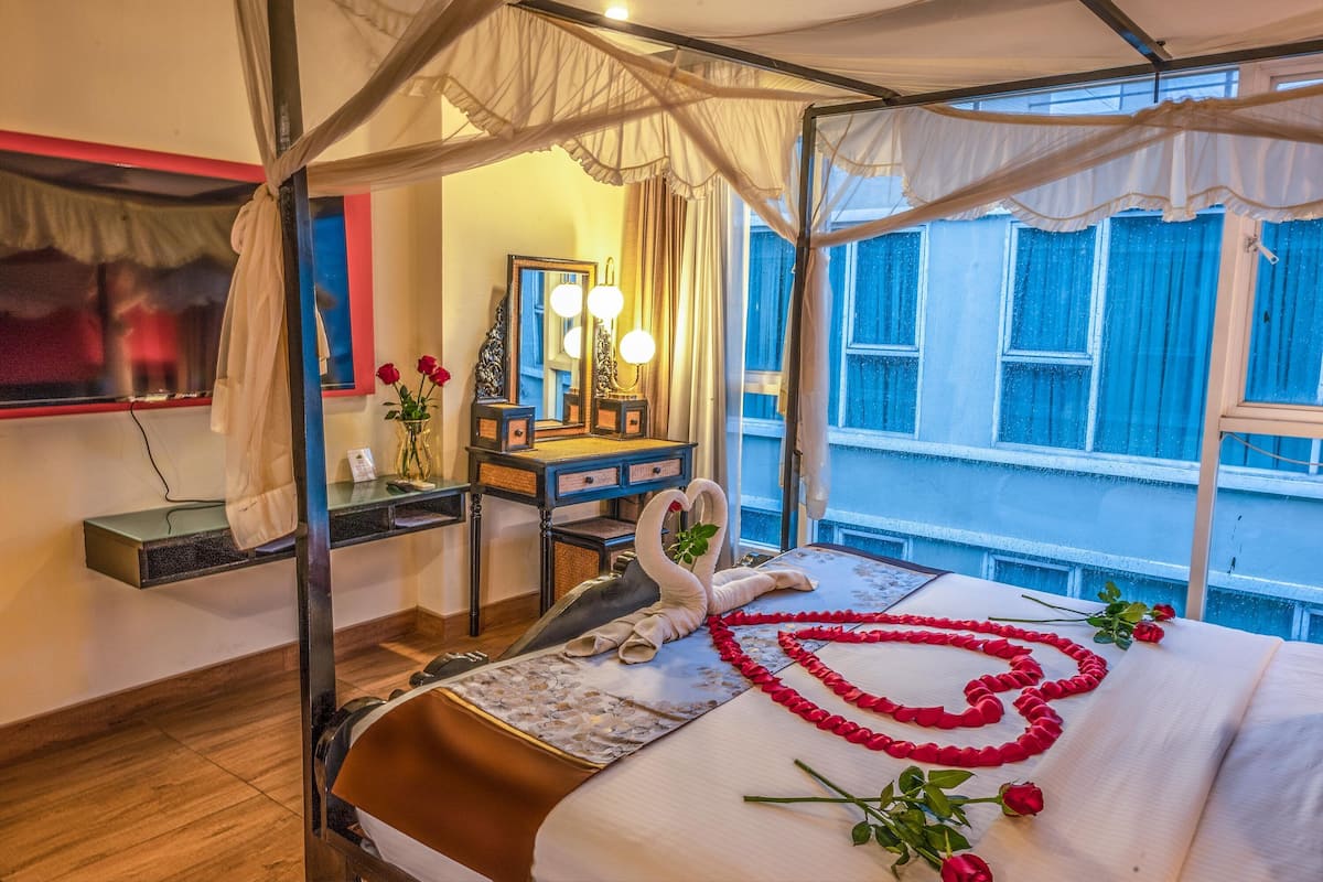 A hotel room with a canopy bed, a desk with a mirror, and a view of the city.