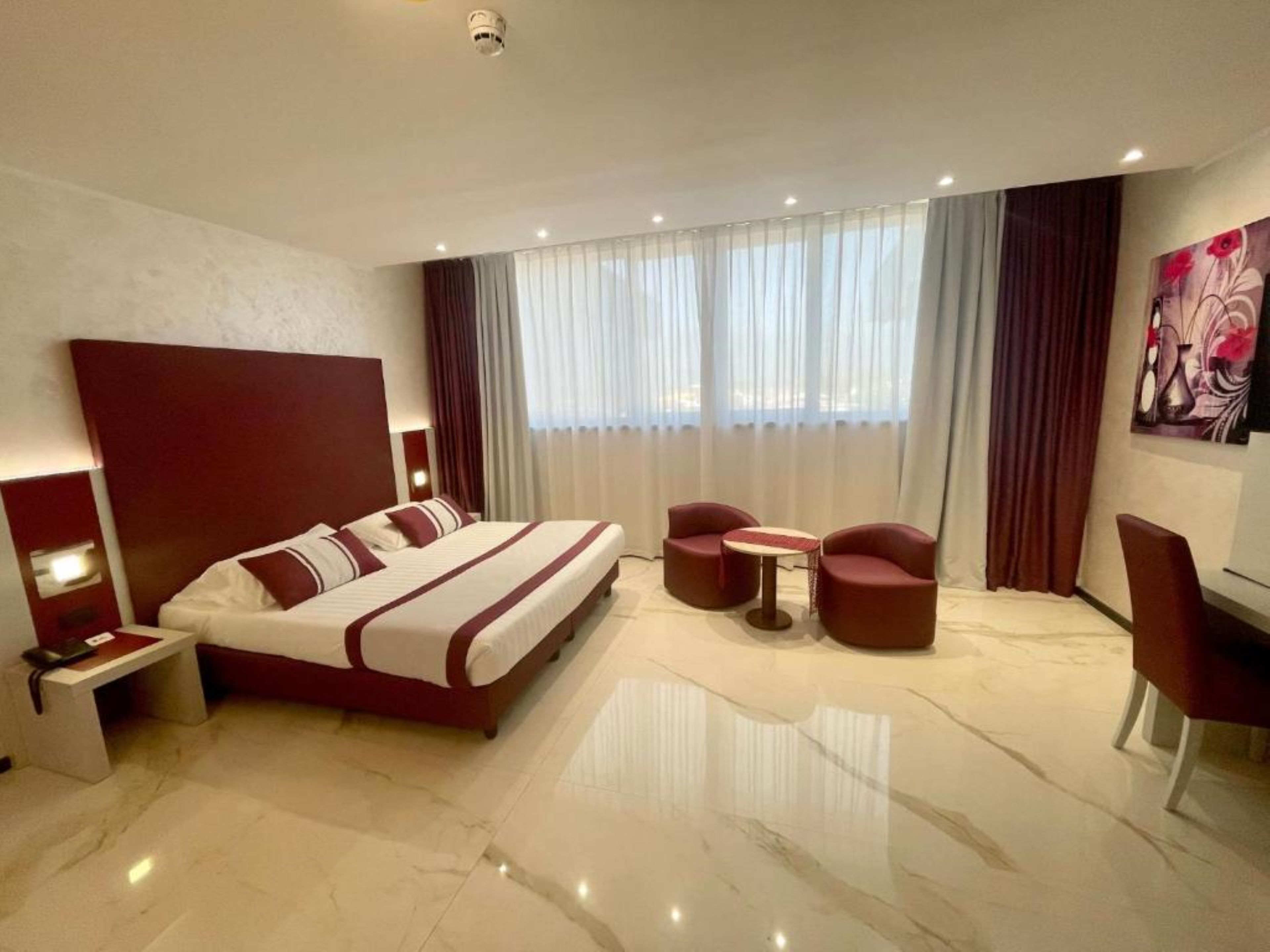 Ein modernes Hotelzimmer mit einem großen Bett, zwei Sesseln, einem kleinen Tisch und einem Schreibtisch mit Stuhl.