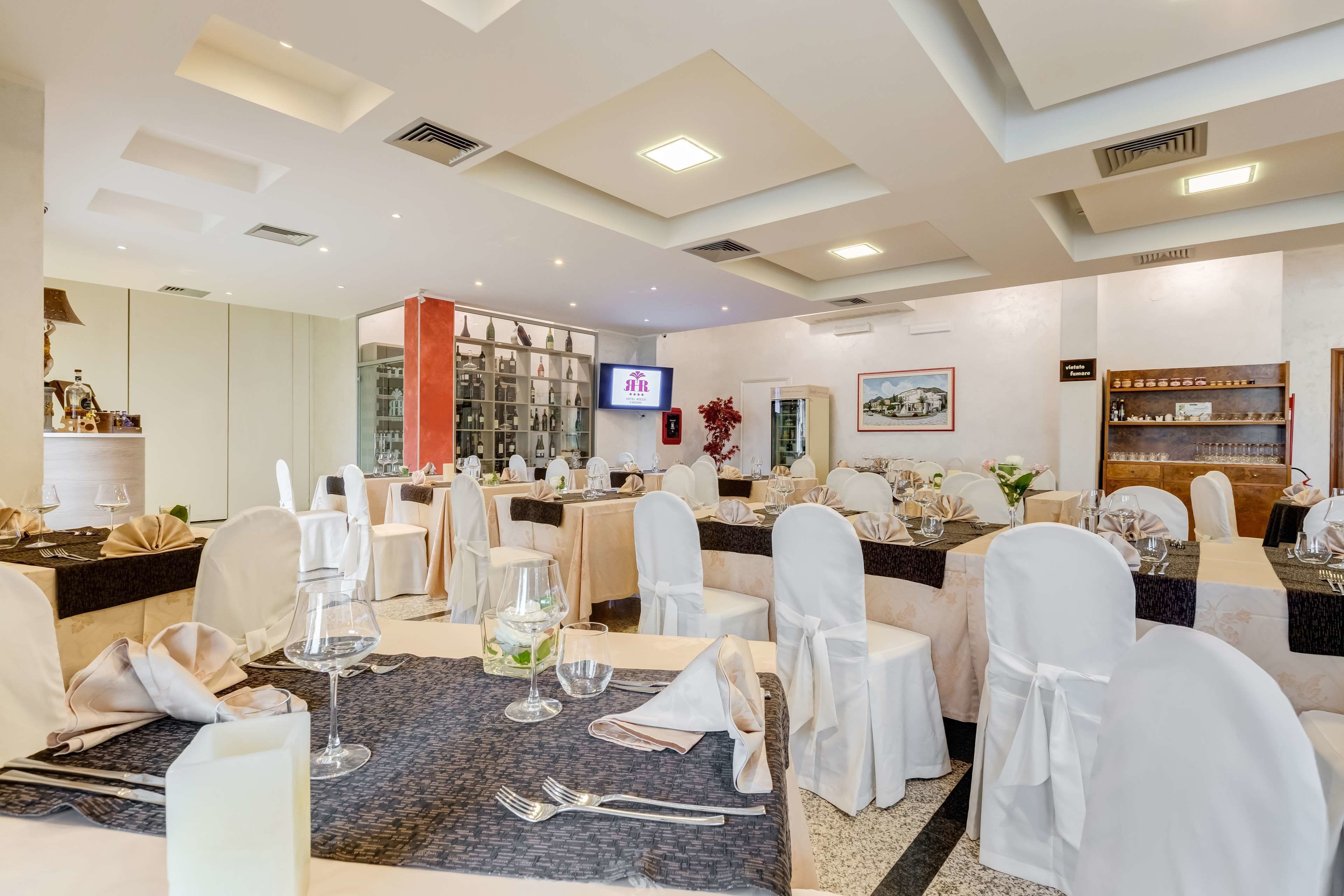 Ein Restaurantbereich eines Hotels mit gedeckten Tischen, einem Fernseher und einer Bar mit Regalen.