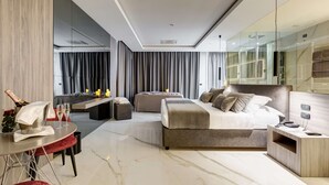 A modern hotel room with a large bed, a sitting area, a dining table, and a minibar.