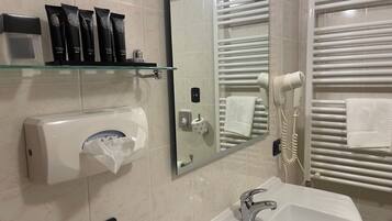 Un baño con lavamanos, espejo, toallero y secador de pelo.