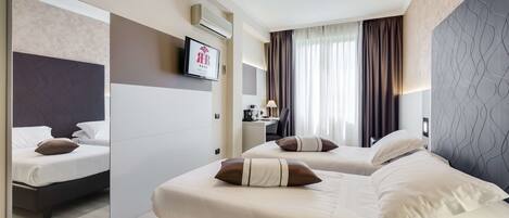 Habitación de hotel moderna con dos camas, un escritorio, un televisor y un espejo grande.