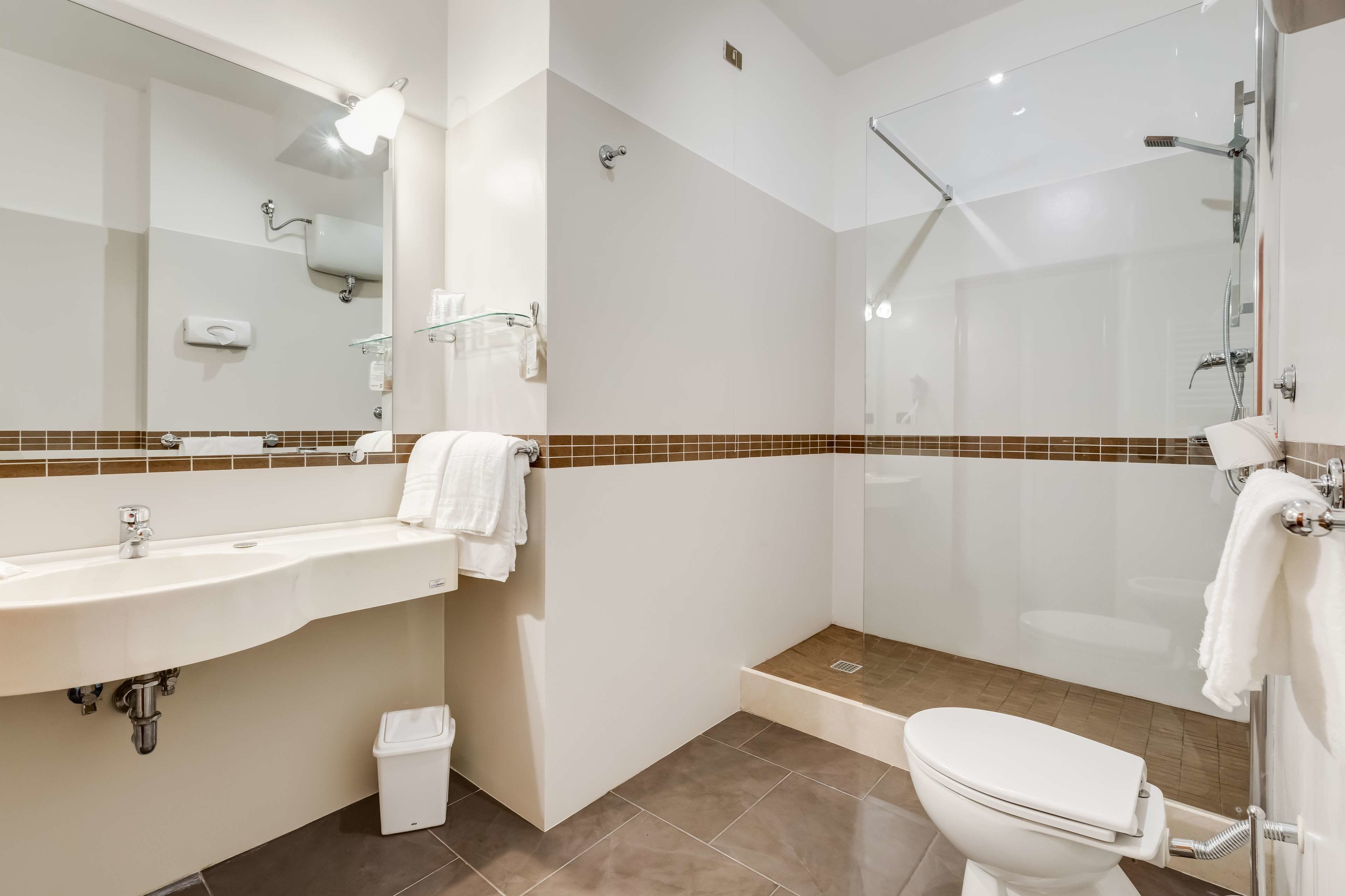 A modern bathroom with a sink, mirror, shower, and toilet.
