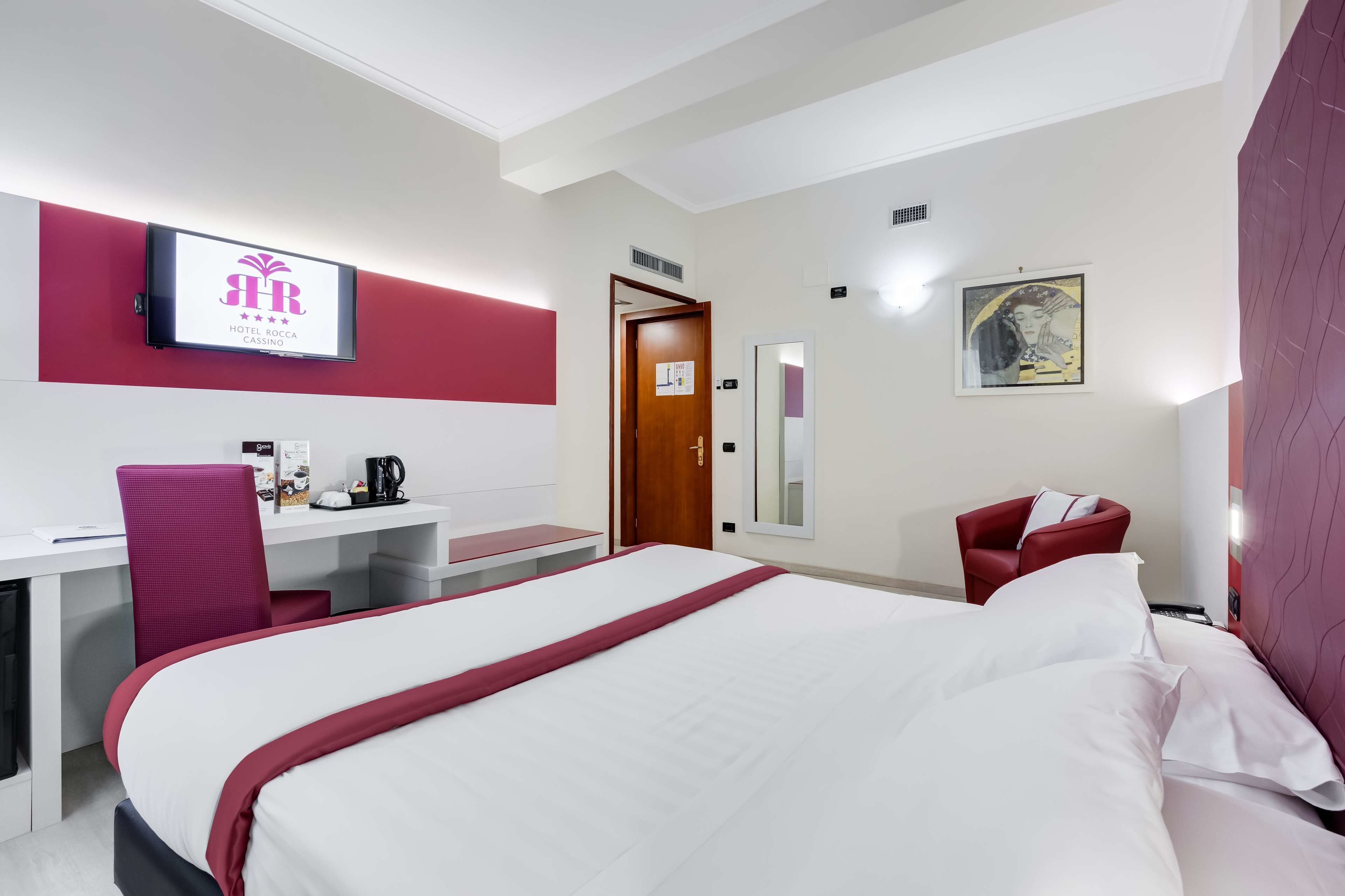 Una habitación de hotel con cama, escritorio, silla, televisor y puerta.