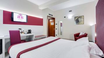 A hotel room with a bed, a desk, a chair, a TV, and a door.