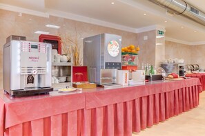 A hotel breakfast area with a long counter, Nescafé machines, a fruit display, and various food items.