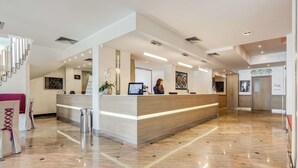 A modern hotel reception area with a marble floor, a reception desk, and a staircase.