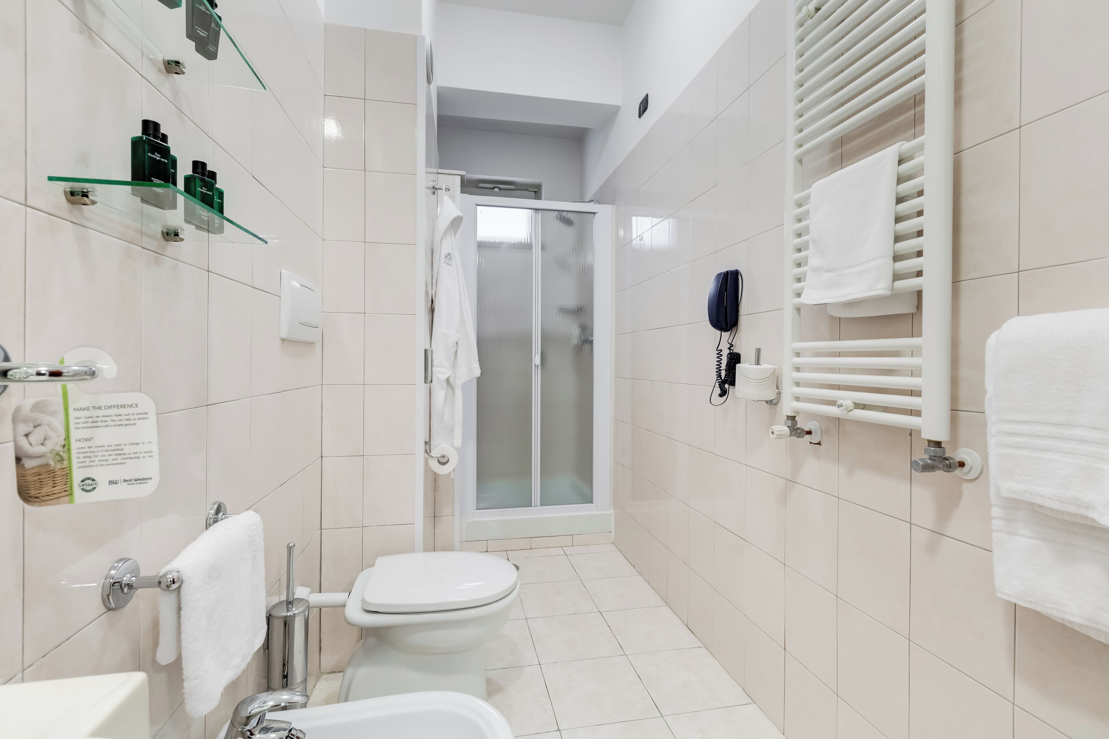 A modern bathroom with a toilet, shower, and glass shelves with toiletries.