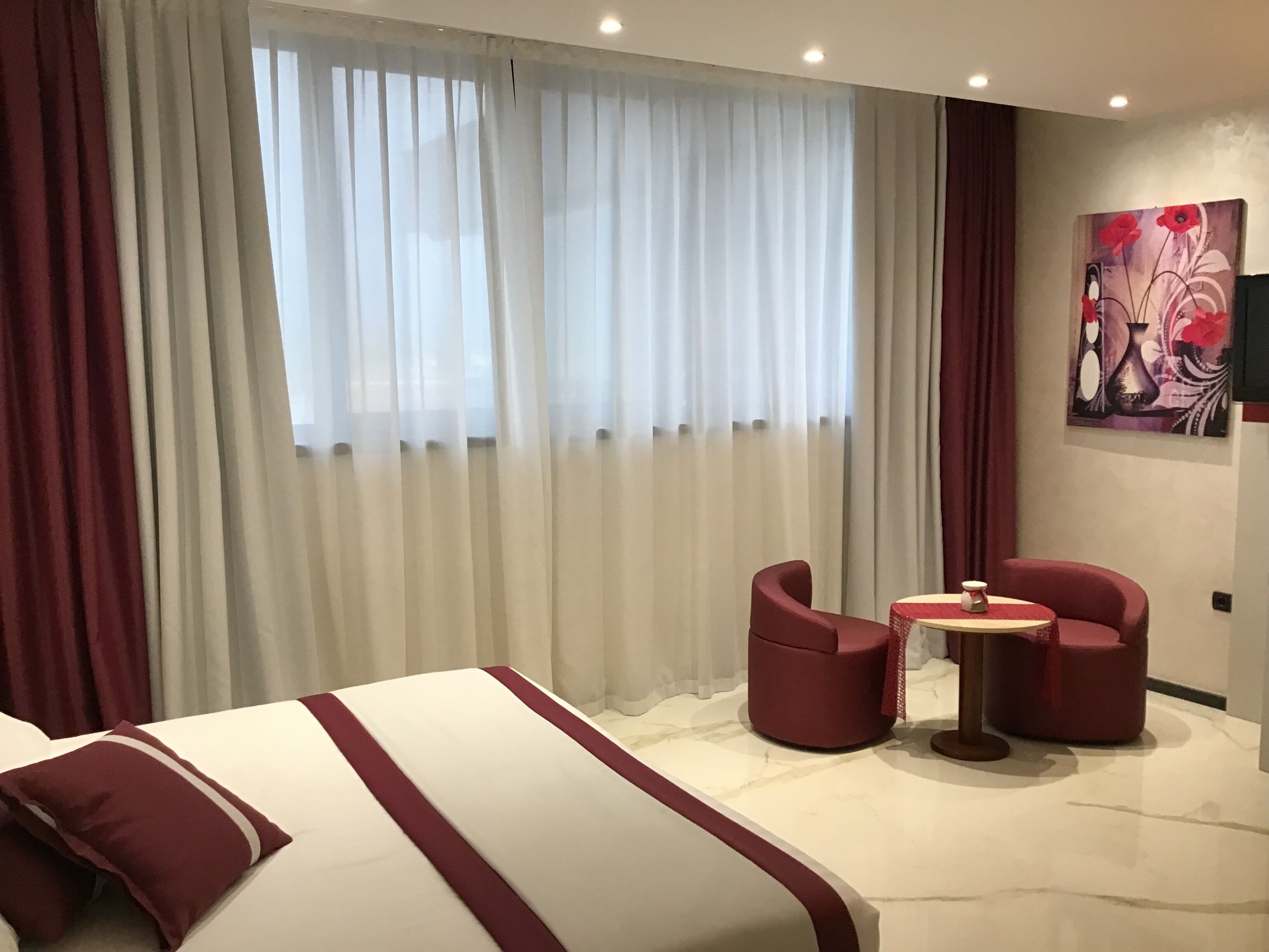 Une chambre d’hôtel avec un lit, deux fauteuils rouges, une petite table et un tableau au mur.