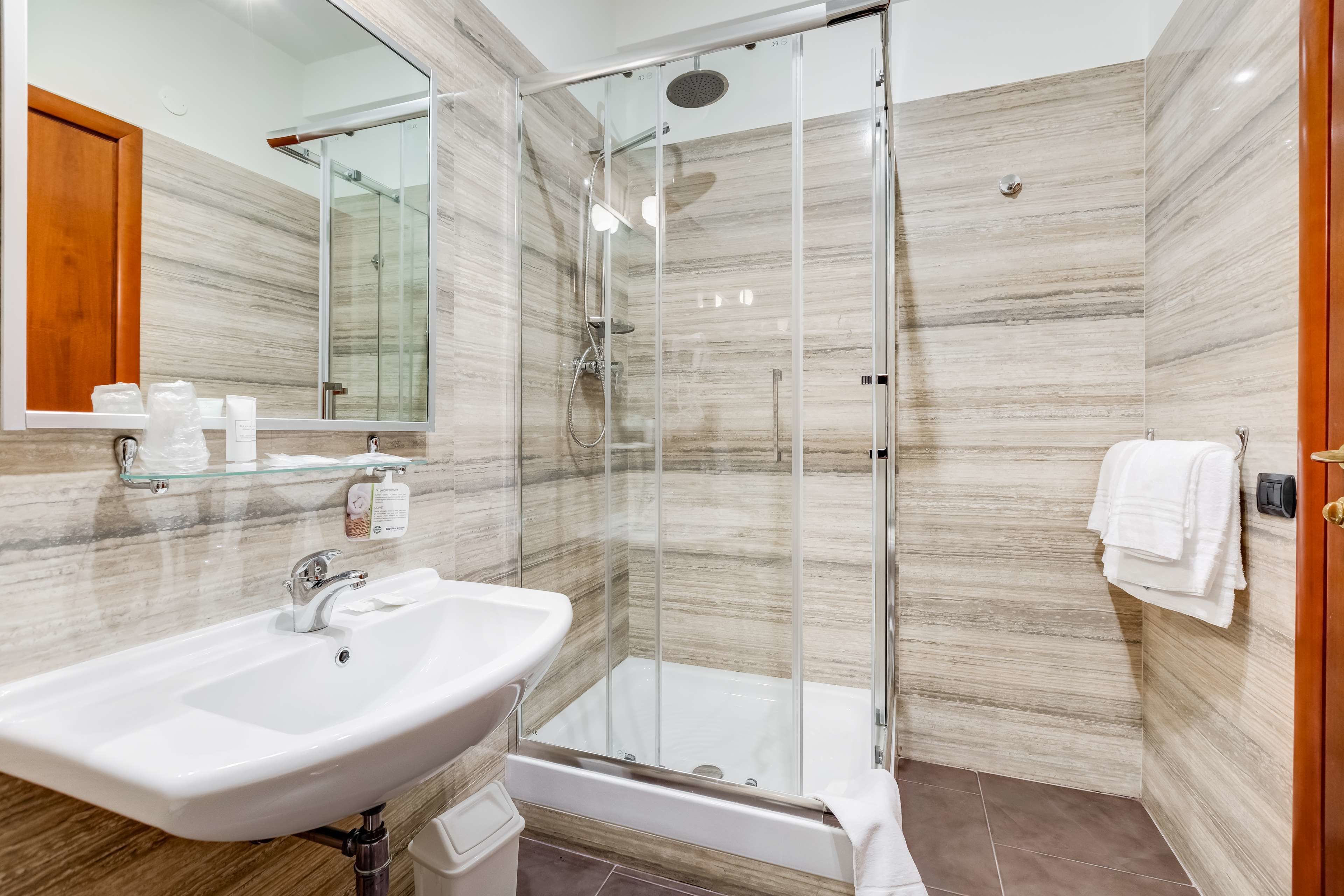 A modern bathroom with a glass-enclosed shower, a white sink, and a large mirror.