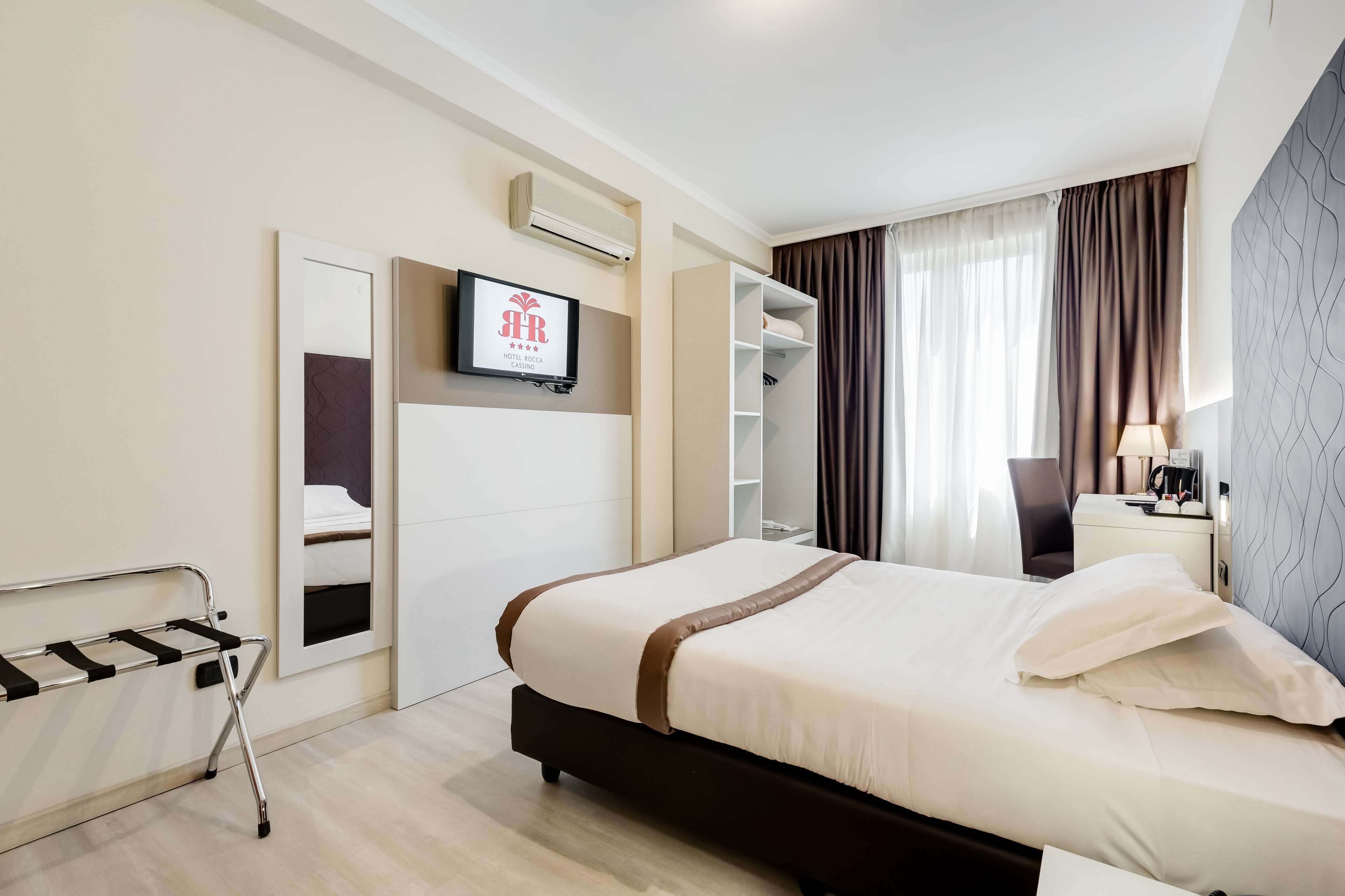 Ein Hotelzimmer mit Bett, Wand-Fernseher, Kleiderschrank und Nachttisch mit Lampe.