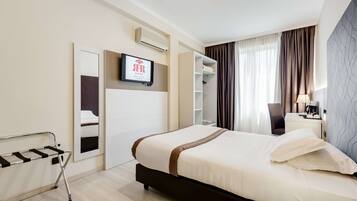 Ein Hotelzimmer mit Bett, Wand-Fernseher, Kleiderschrank und Nachttisch mit Lampe.