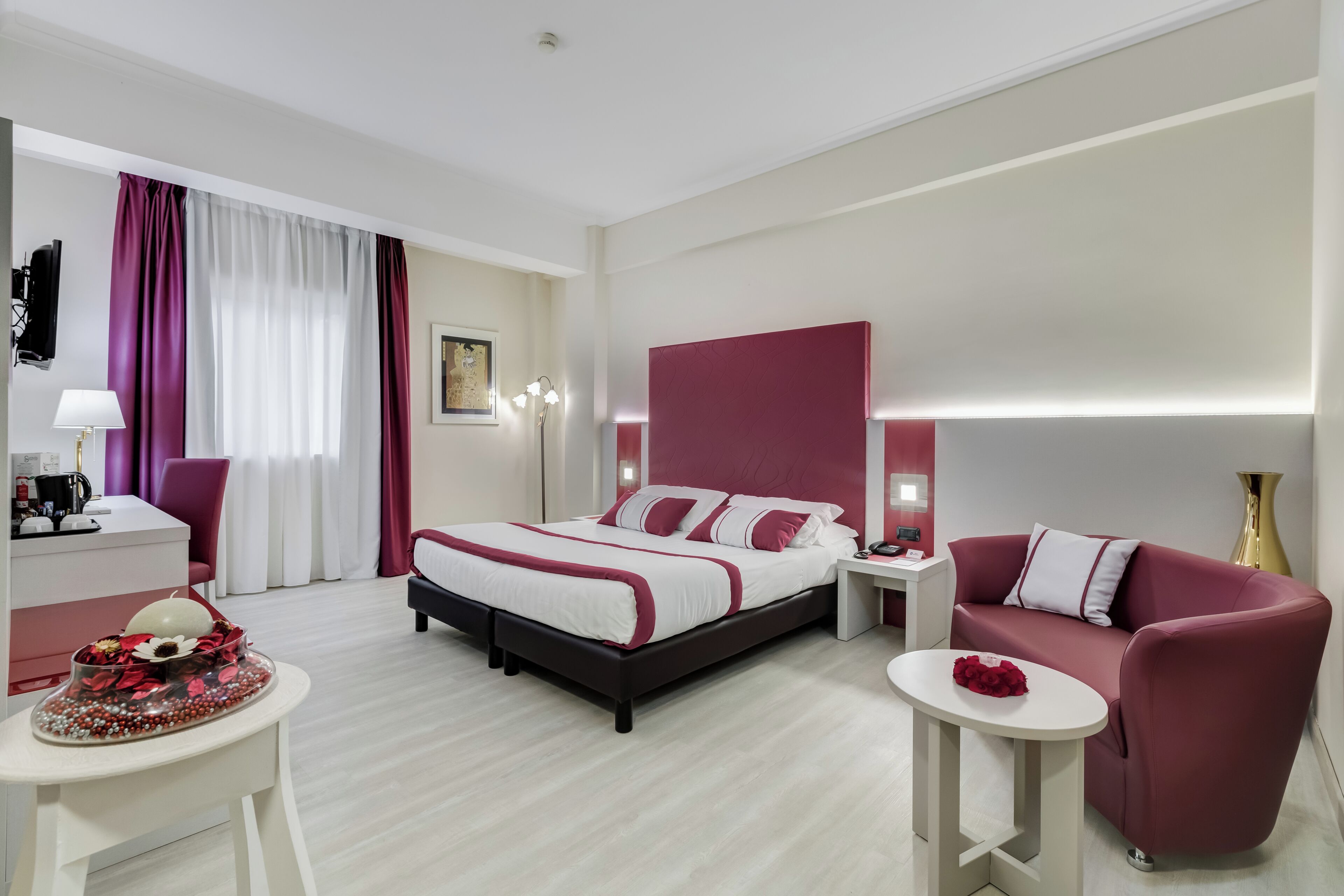 A modern hotel room with a bed, a sofa, a desk, and a small table.