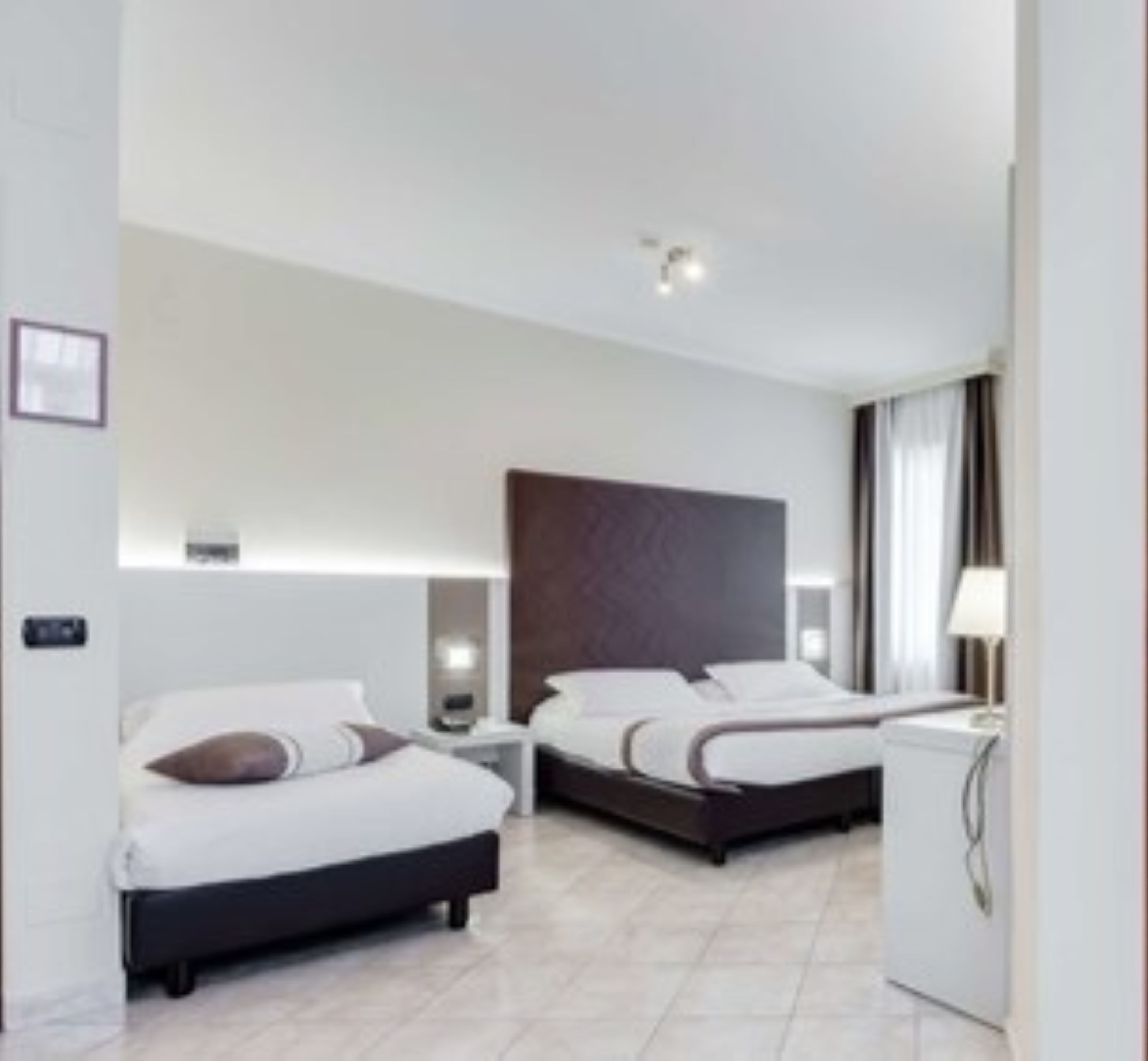 Una camera d'albergo moderna con due letti, una scrivania e un comodino.