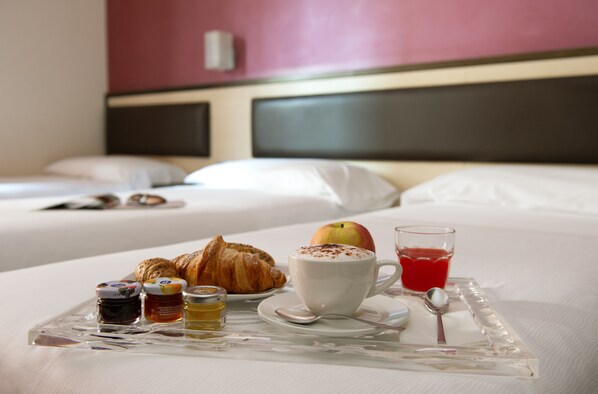 A breakfast tray with croissants, a cup of coffee, an apple, and a glass of red juice on a hotel bed. - Hotel Five (Milan)