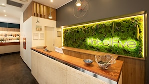 A reception area with a wooden counter, a green wall with 'HotelLive' illuminated, and a clock above. - Hotel Five (Milan)