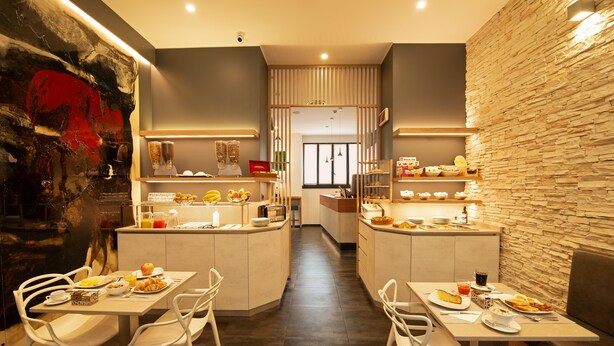 A modern dining area with a central island, white chairs, and a variety of food items displayed on shelves. - Hotel Five (Milan)