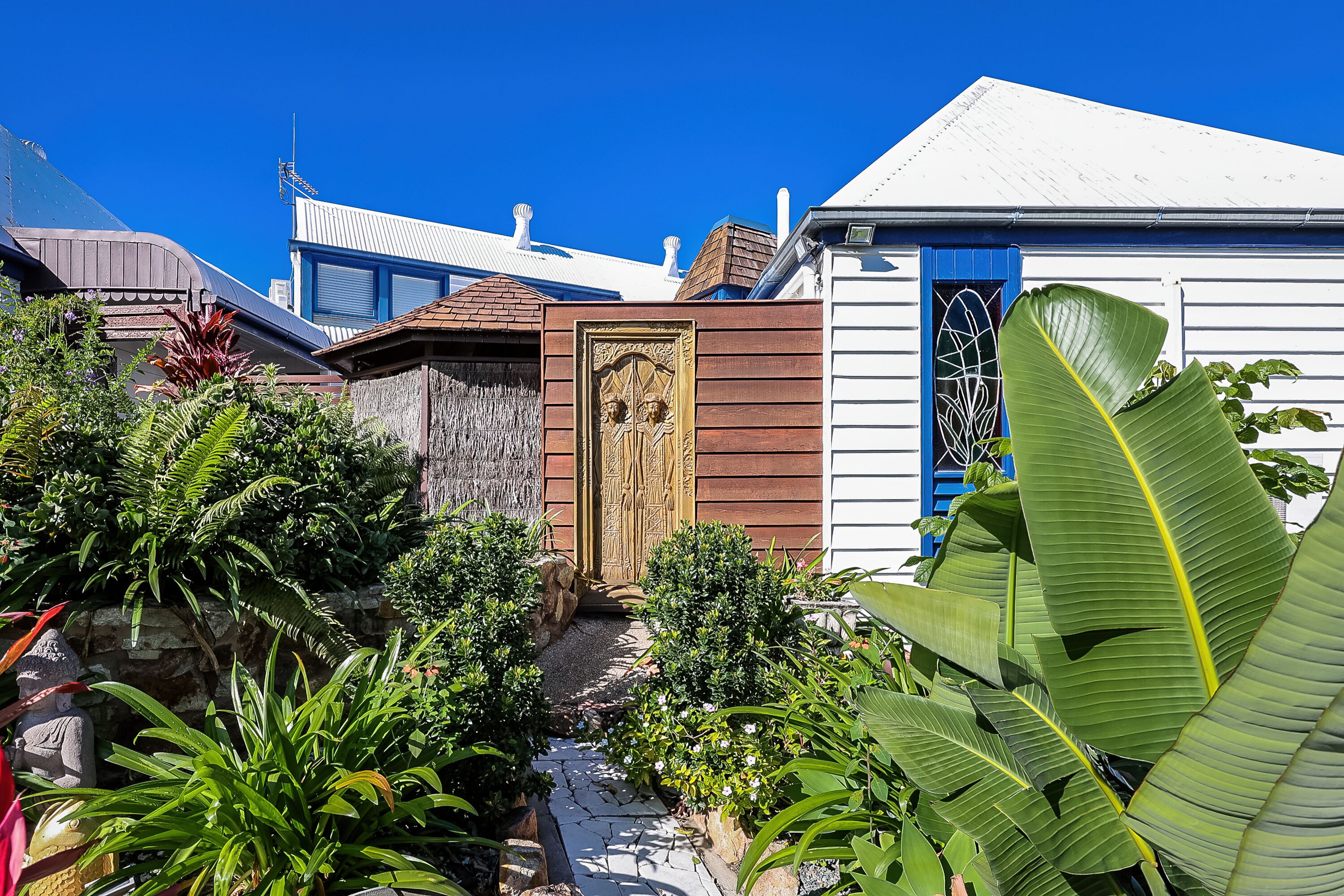 A garden with a stone wall, a wooden door, and various plants.