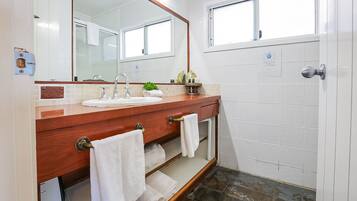 Un baño con tocador de madera, lavamanos blanco y un espejo grande. Hay toallas colgadas en el tocador y una ventana sobre el lavamanos.