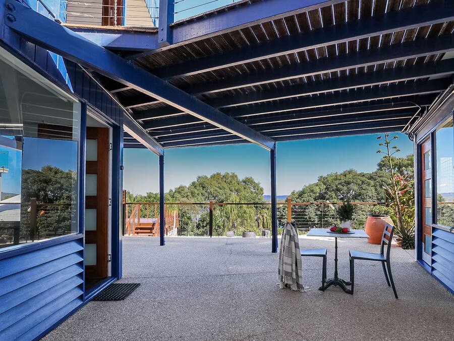 A covered outdoor area with a table and chairs, a large potted plant, and a view of trees and hills.