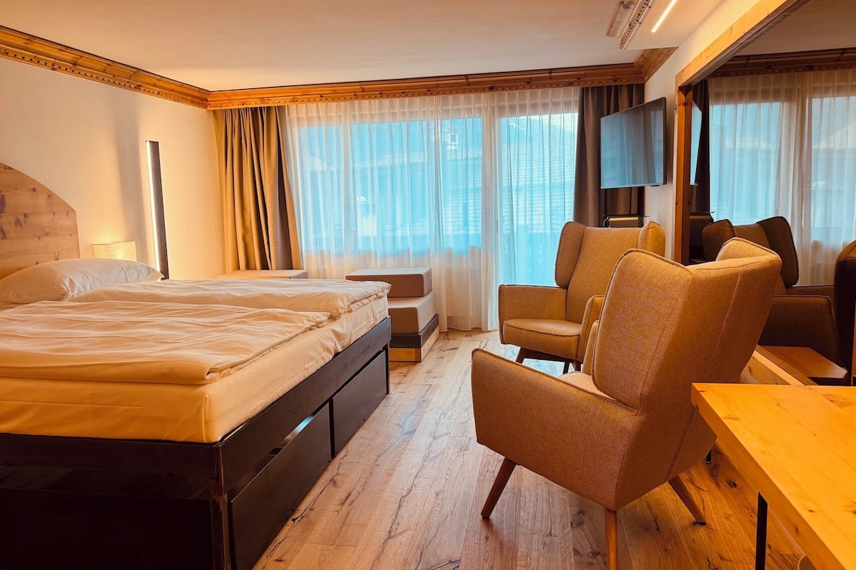 A hotel room with a bed, a sofa, a TV, and a view of the city.