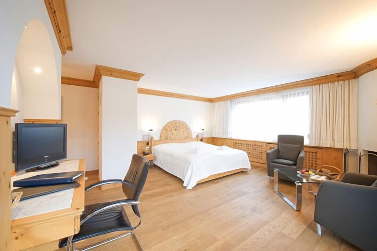 A hotel room with a bed, a desk with a computer, a chair, and a television.
