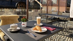 Een gedekte tafel met een croissant, een kop koffie en een glas bier, met een bergzicht op de achtergrond.