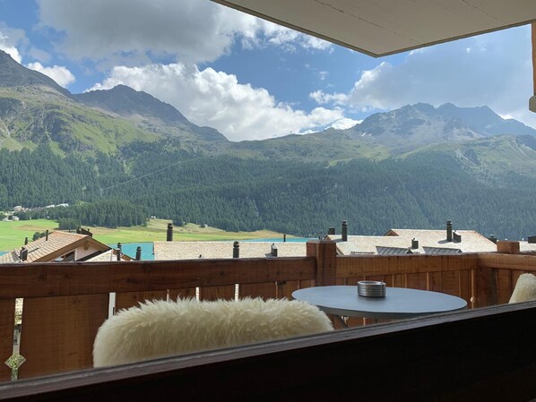 A wooden deck with a round table and a white furry rug, overlooking a mountainous landscape with a clear sky. - Albana Hotel Silvaplana (Silvaplana)