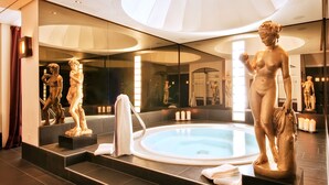 Een moderne spa met een jacuzzi, marmeren treden en klassieke beelden.