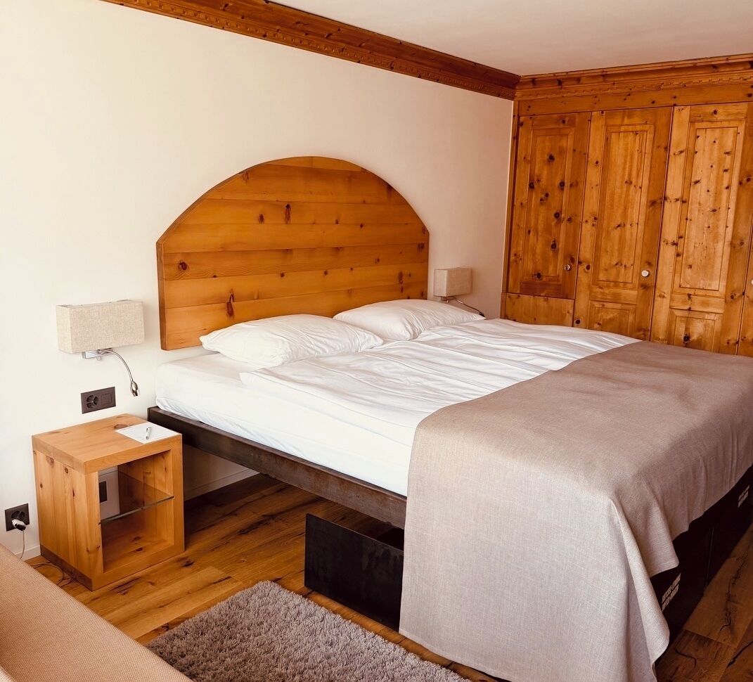 Una cama individual con cabecera de madera, una mesita de noche con lámpara y un armario con detalles de madera.