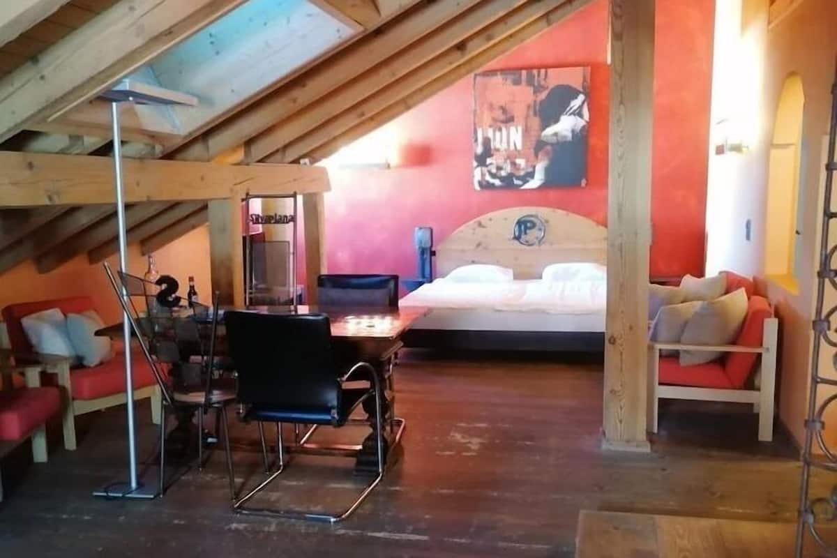 A cozy attic room with a bed, a red couch, and a dining table.