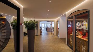 A hotel corridor with a bar on the right, a staircase on the left, and a large plant in the center.