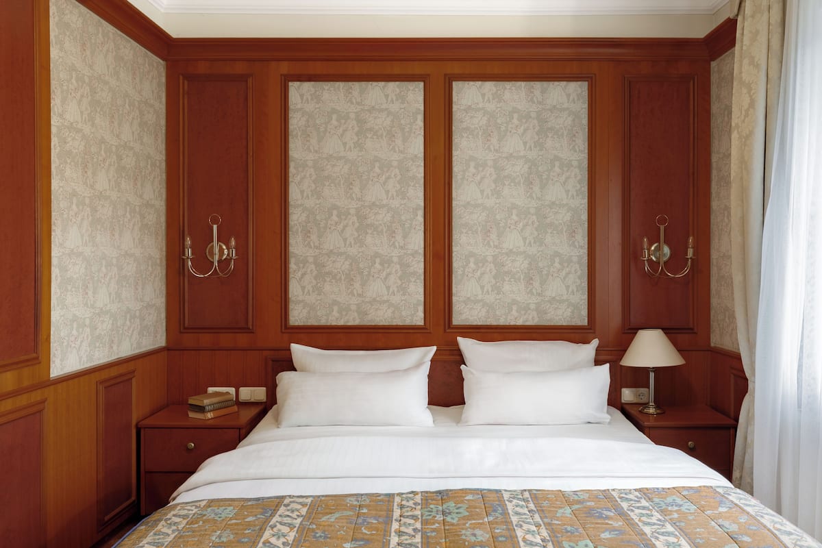Ein Hotelzimmer mit einem großen Bett, zwei Nachttischen, einer Lampe und einer gemusterten Tagesdecke.