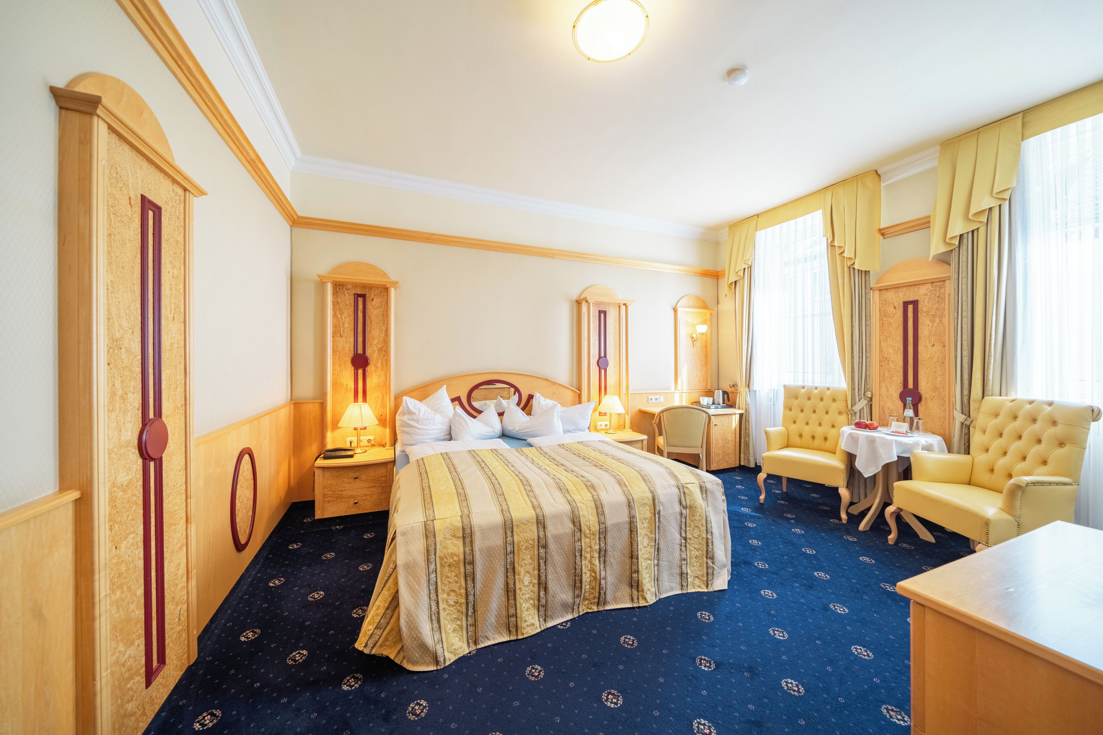 Ett hotellrum med en stor säng, två fåtöljer, ett litet bord och ett skrivbord.