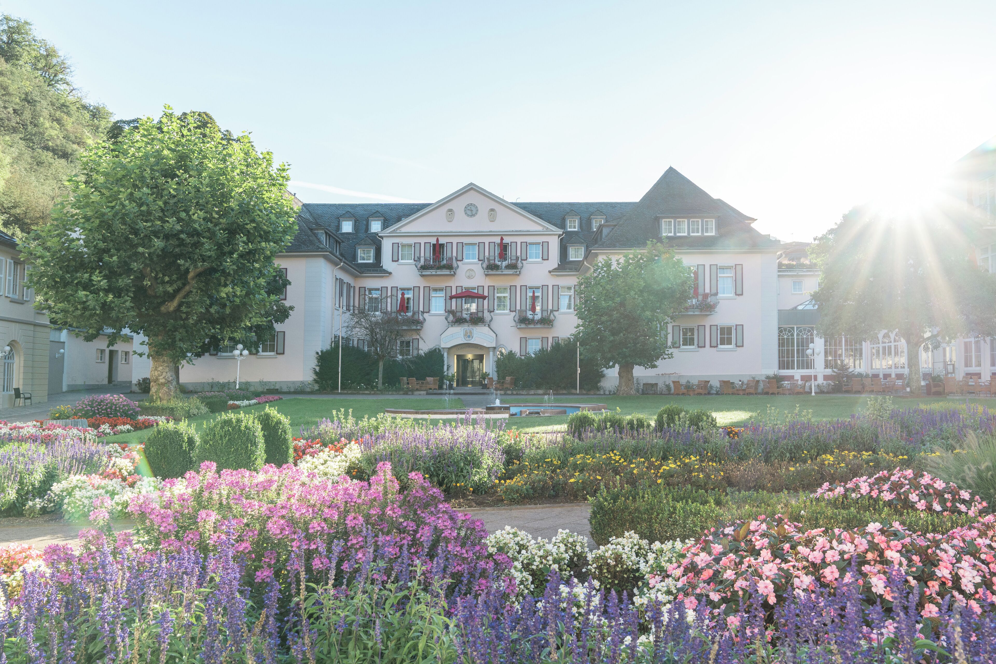 A large, stately building with a symmetrical facade, a central entrance, and a formal garden with various flower beds.