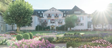 A large, stately building with a symmetrical facade, a central entrance, and a formal garden with various flower beds.