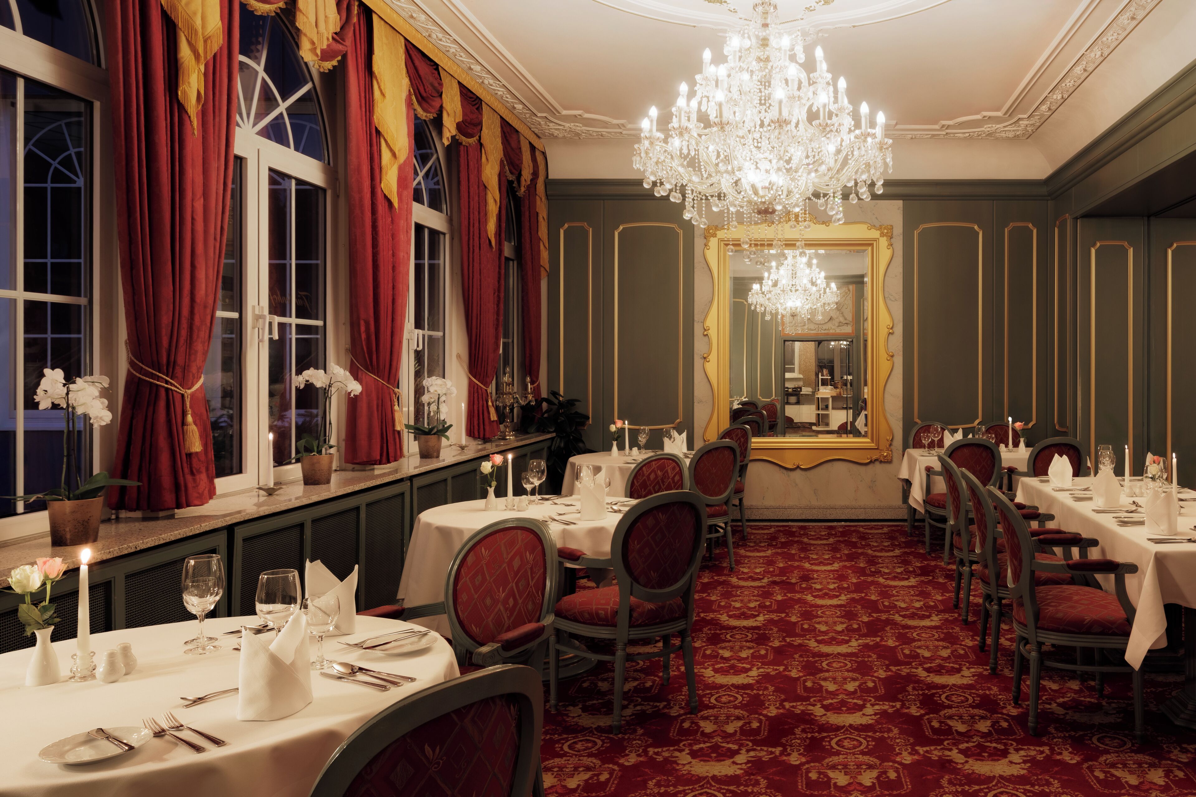 Un comedor formal con mesas dispuestas para el servicio, una araña y un espejo grande.
