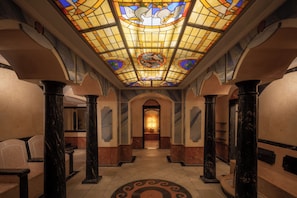 A hallway with a stained glass ceiling, marble columns, and a patterned floor.