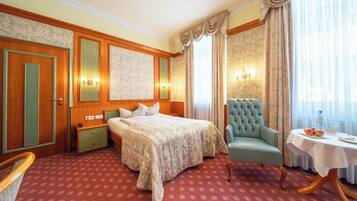 Habitación de hotel con cama, una silla, una mesa con botella y vasos, y ventana con cortinas.