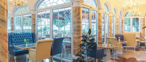 A luxurious lobby with marble columns, blue upholstered seating, and large windows offering views of the outdoors.