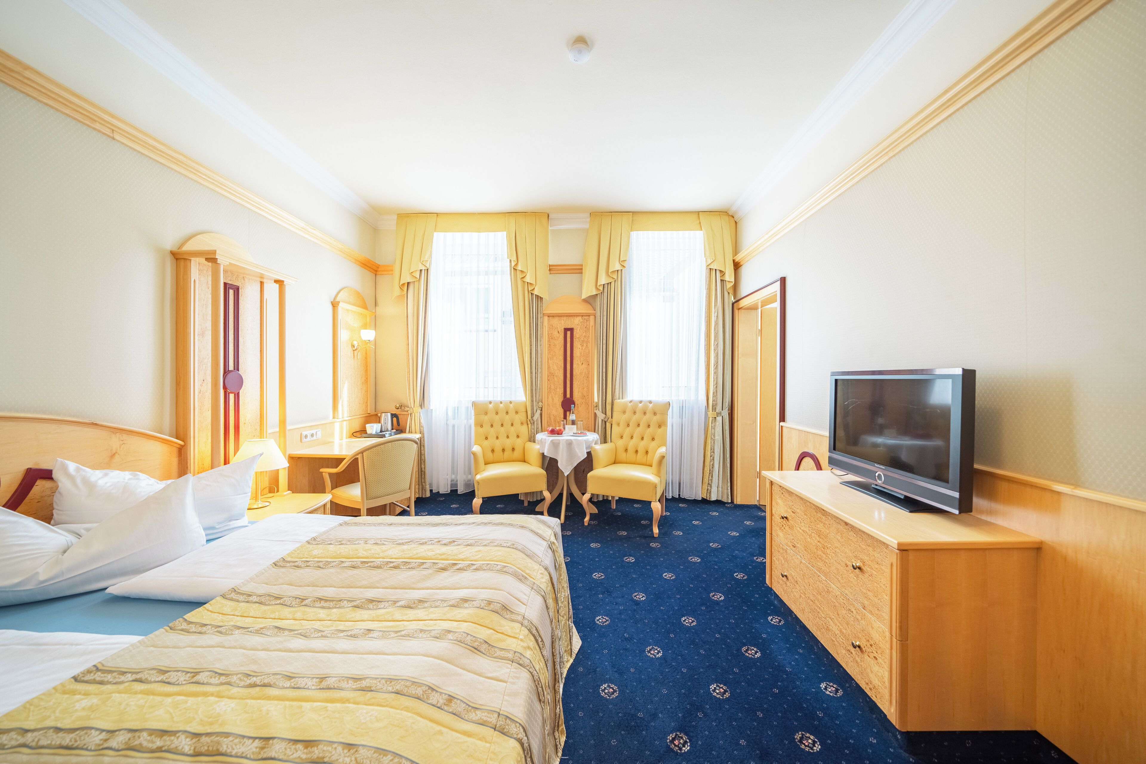 Una habitación de hotel con cama, escritorio, dos sillas, televisor y una mesita.