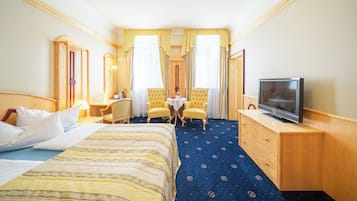 Ett hotellrum med en säng, ett skrivbord, två stolar, en tv och ett litet bord.