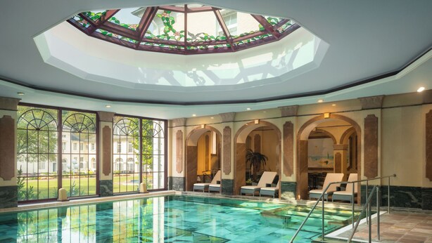 A large indoor swimming pool with a glass floor, surrounded by lounge chairs and a skylight. - Hotel Fürstenhof Bad Bertrich (Bad Bertrich)