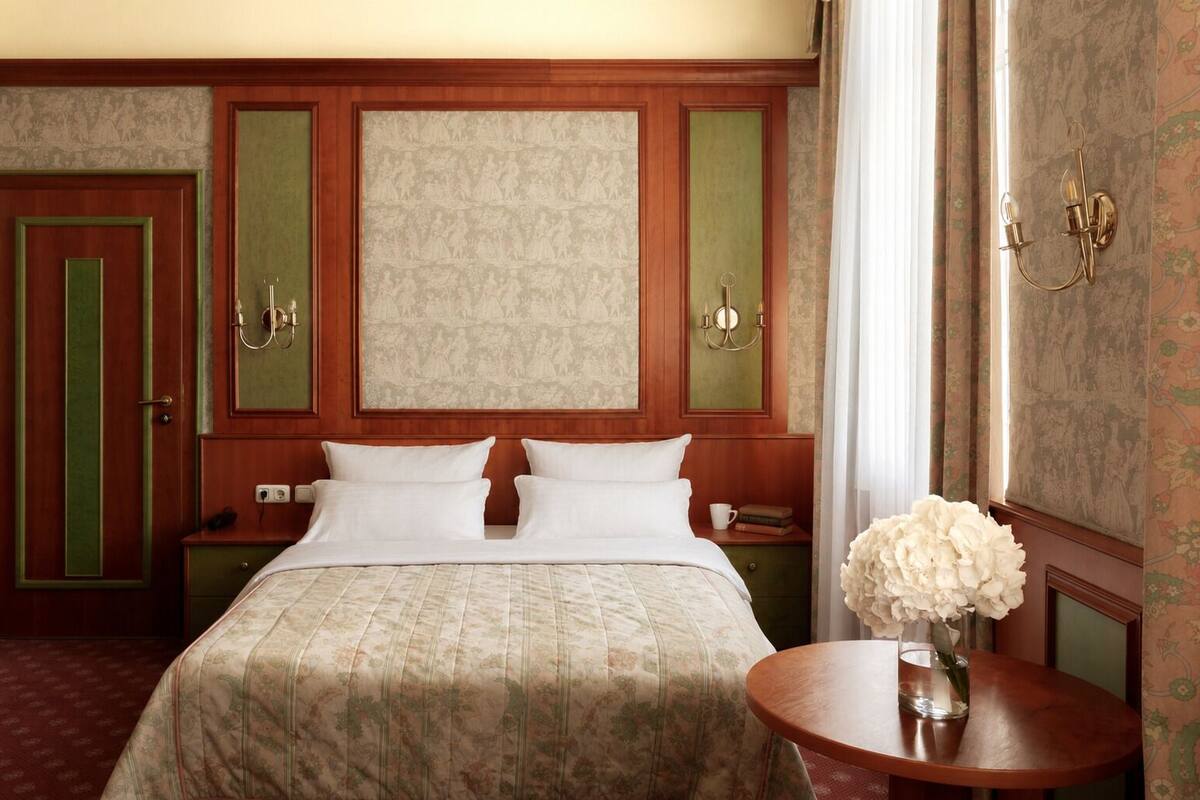 Ein Hotelzimmer mit einem Bett, zwei Nachttischen, einer Lampe und einer Vase mit Blumen.