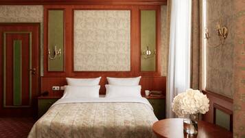 Una habitación de hotel con una cama, dos mesitas de noche, una lámpara de noche, un florero con flores y un aplique de pared.