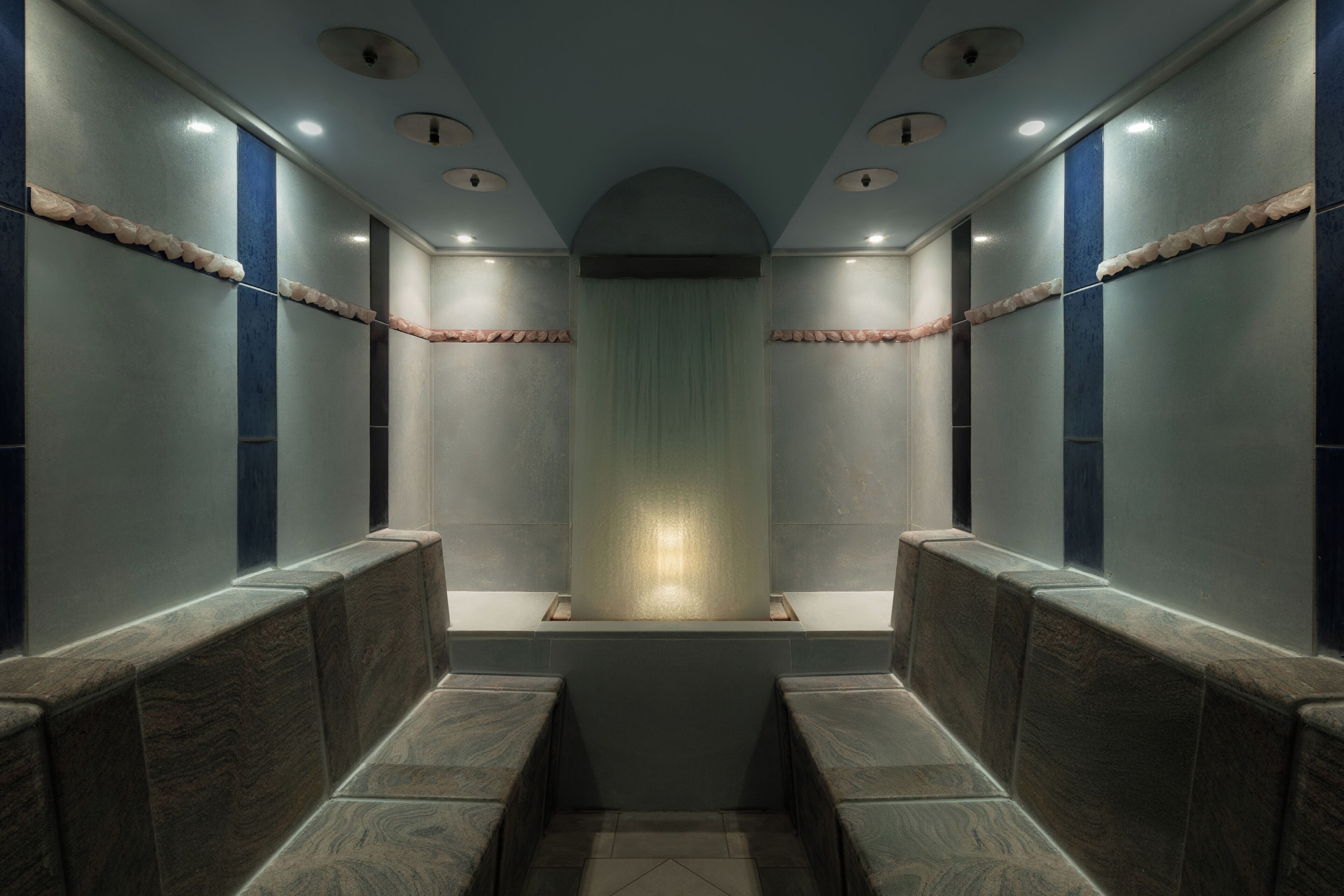 A modern bathroom with a central mirror, recessed lighting, and benches along the walls.