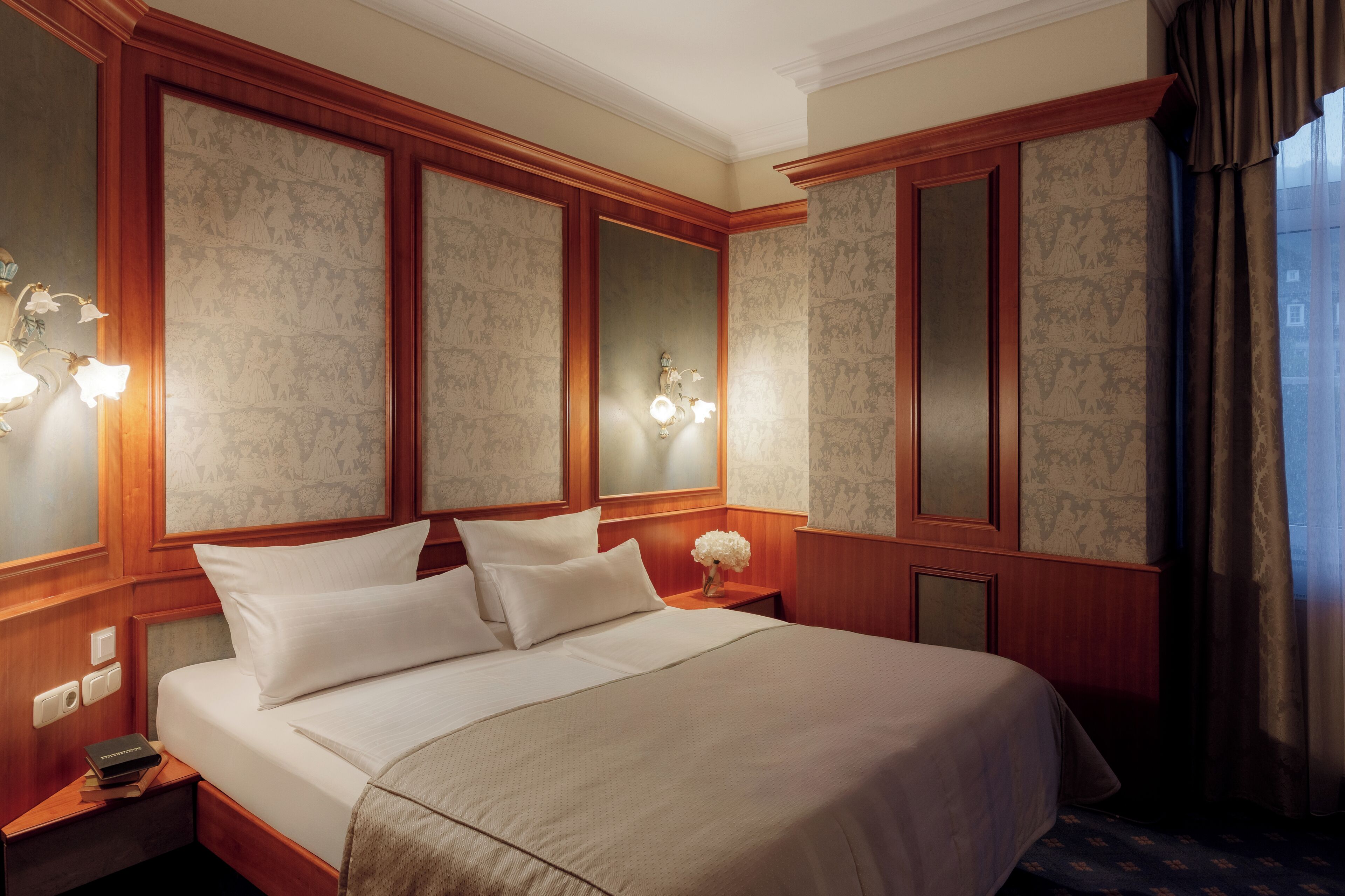 Ein Hotelzimmer mit einem großen Bett, Holzvertäfelung, einem Nachttisch mit einem Buch und einer Wandleuchte.