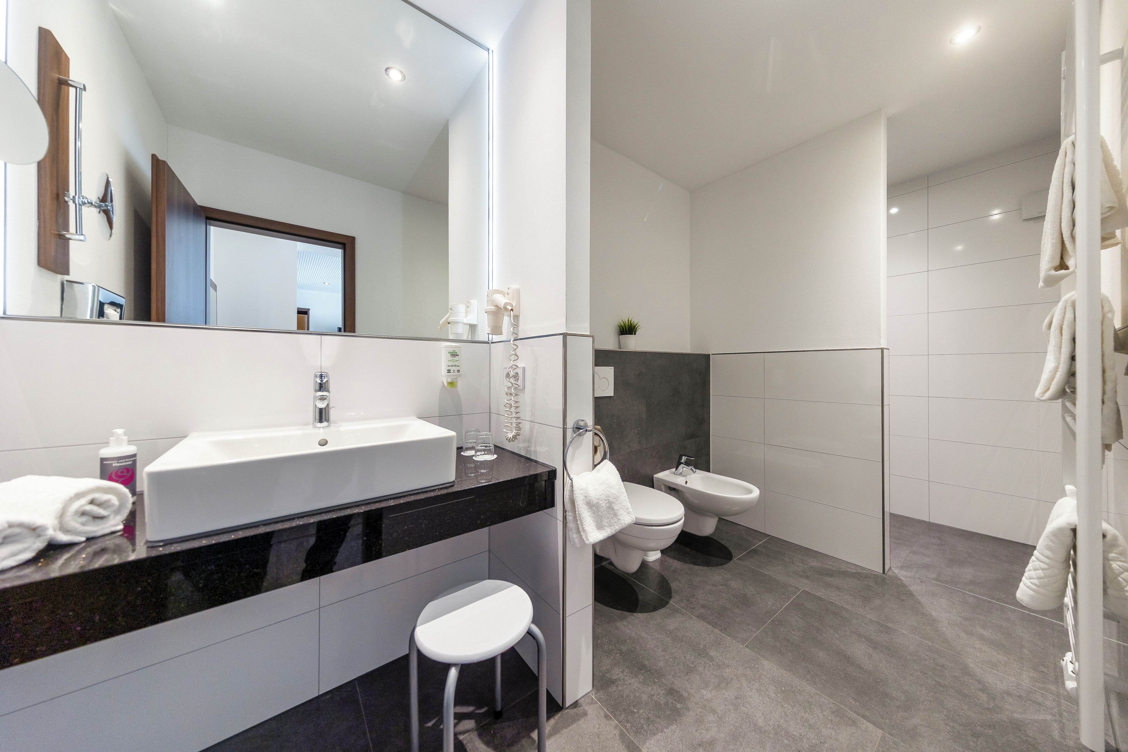A modern bathroom with a large mirror, white sink, and two toilets.